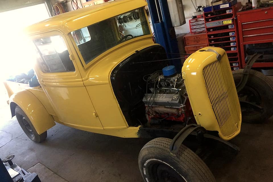 A car with its hood off inside the shop, red tool chests behind
