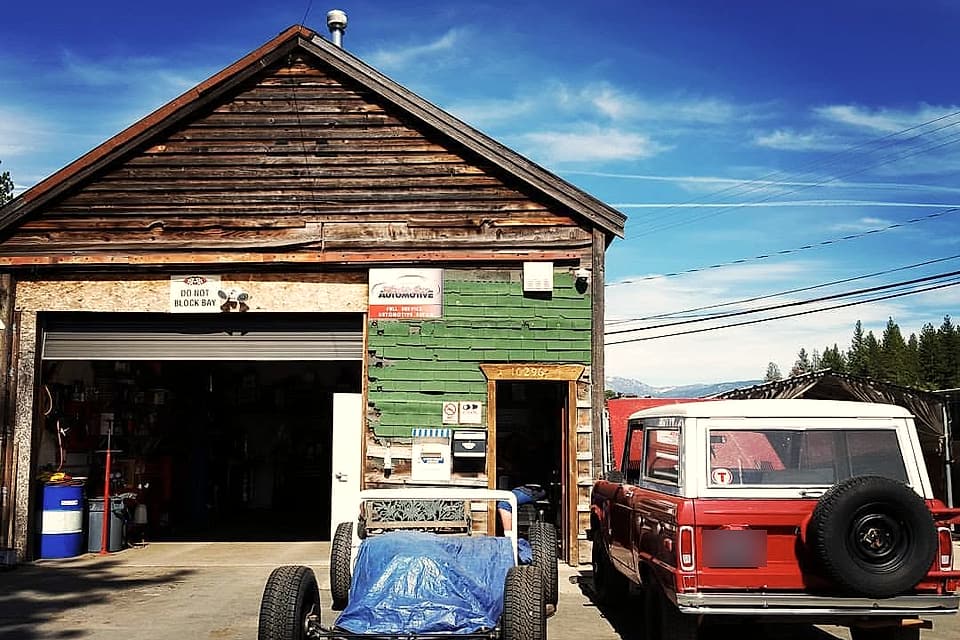The shop front: wood siding, green shingles, the bay door open and a red Bronco parked outside